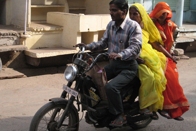 女性をふたり乗せて走るインド人